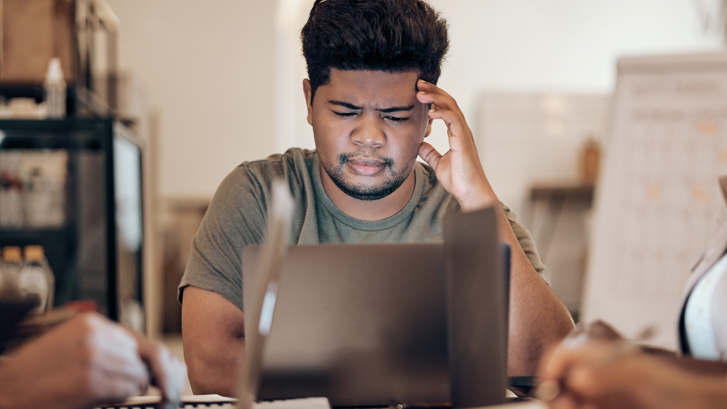 One man is frowning while working on a laptop, his hand against his head.