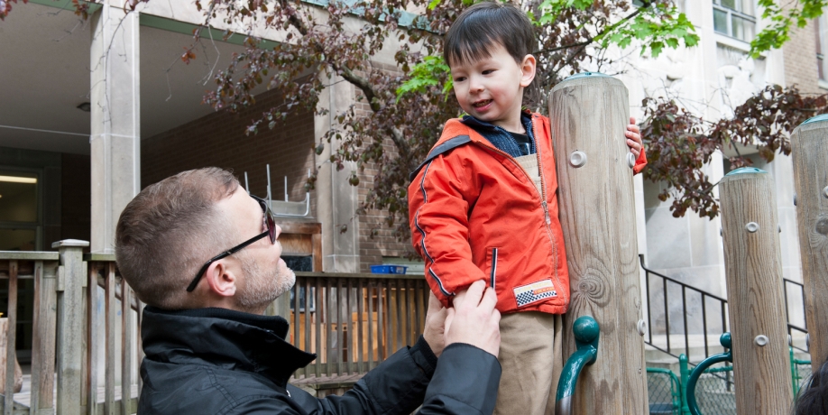 A man with glasses assists a child on the playground