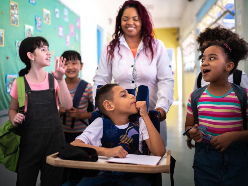 Teacher and students walking in the corridor at school, including a child using a wheelchair