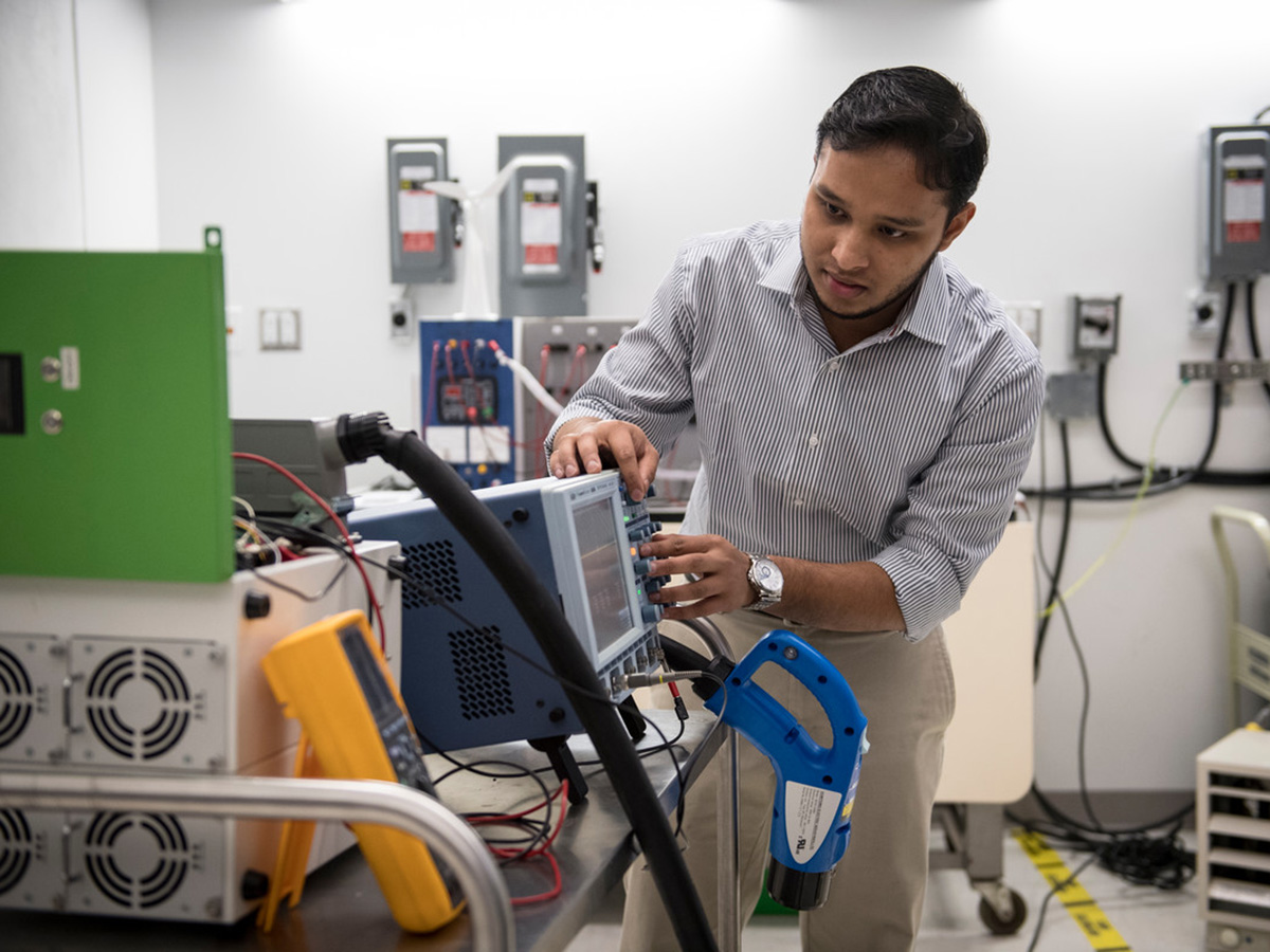 A graduate student works on an electronic machine in a laboratory. 