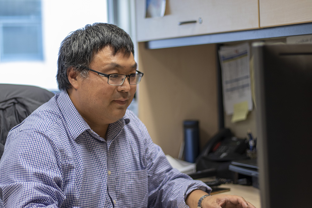 Professor David Xu sits at his desk in his office.