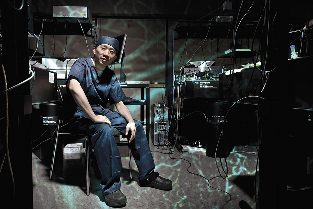 Professor Victor Yang sits in his research laboratory wearing hospital scrubs and a scrub cap.