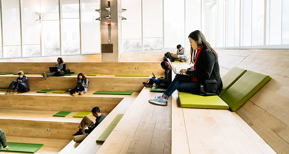 A student sitting with a laptop on the first floor of the Student Learning Centre building. 