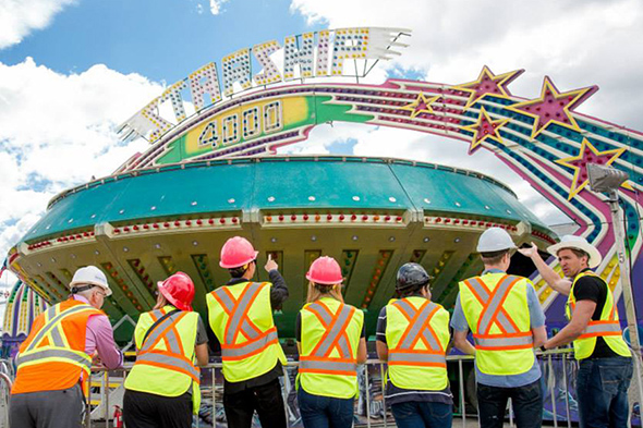 Members of the Ryerson Thrill Club in hard hats and yellow safety vests looking at a carnival ride.