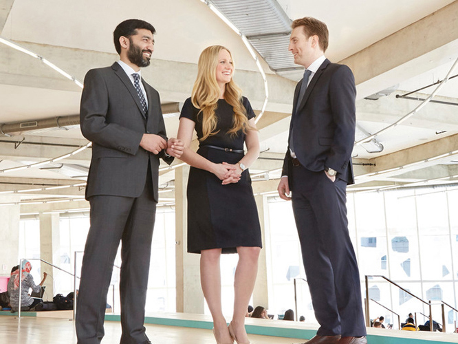 Three students in business formal attire chat together. 