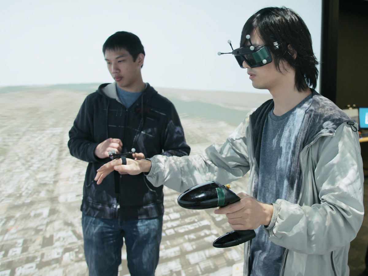 A student wears an augmented reality headset and holds a controller in front of a screen.