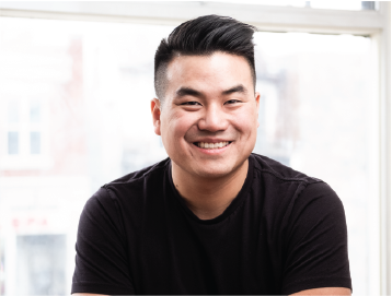 Jason, dark hair wearing a black t-shirt sits in front of a bright window. The background is softly blurred, conveying a warm, relaxed atmosphere.