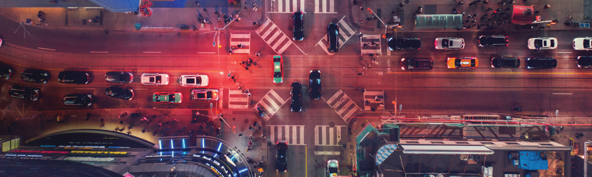 Birds-eye view of a street in downtown Toronto. There is a red glow across the street with many cars and taxis driving.