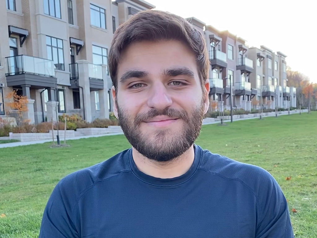 Jake Kroft smiling on the green-space surrounding an apartment complex