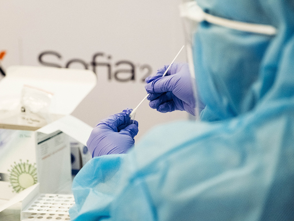 Nurse wearing Personal Protective Equipment (PPE) places a swab into a tube