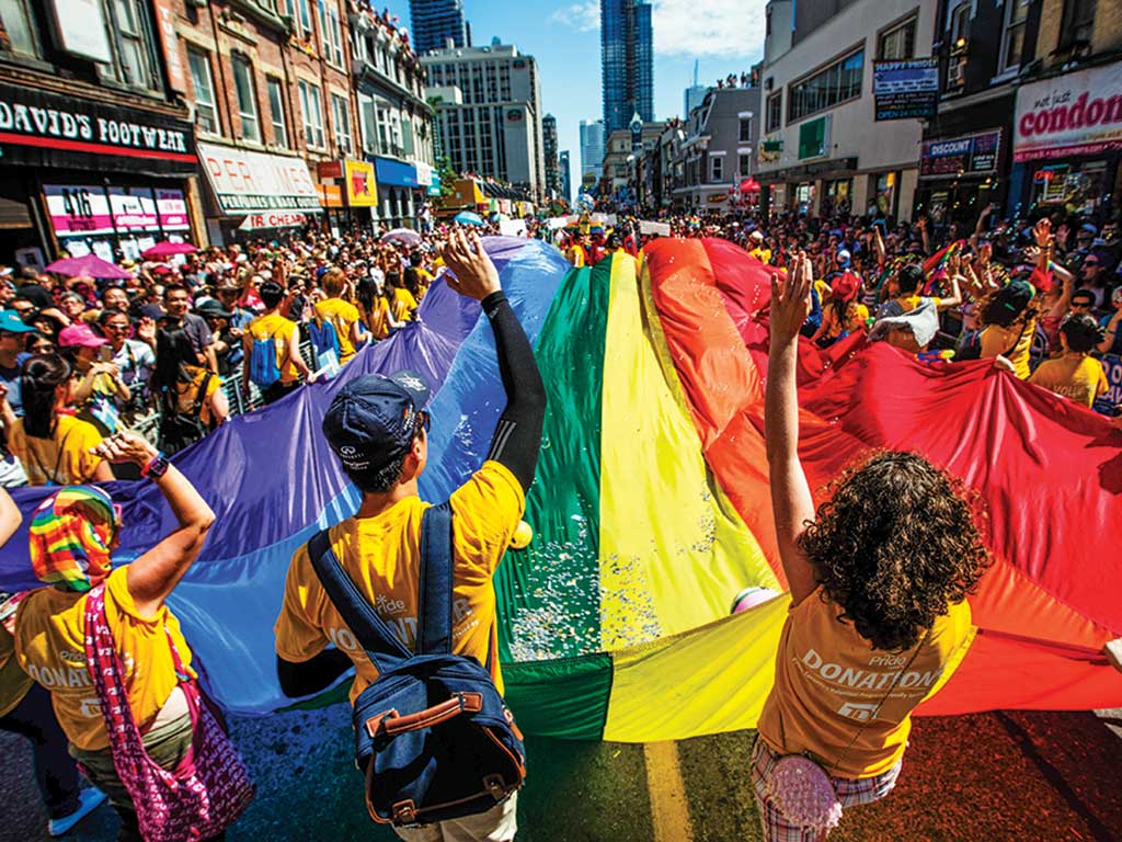 A rainbow flag is held and stretched  by many people down a city street during Pride Parade 