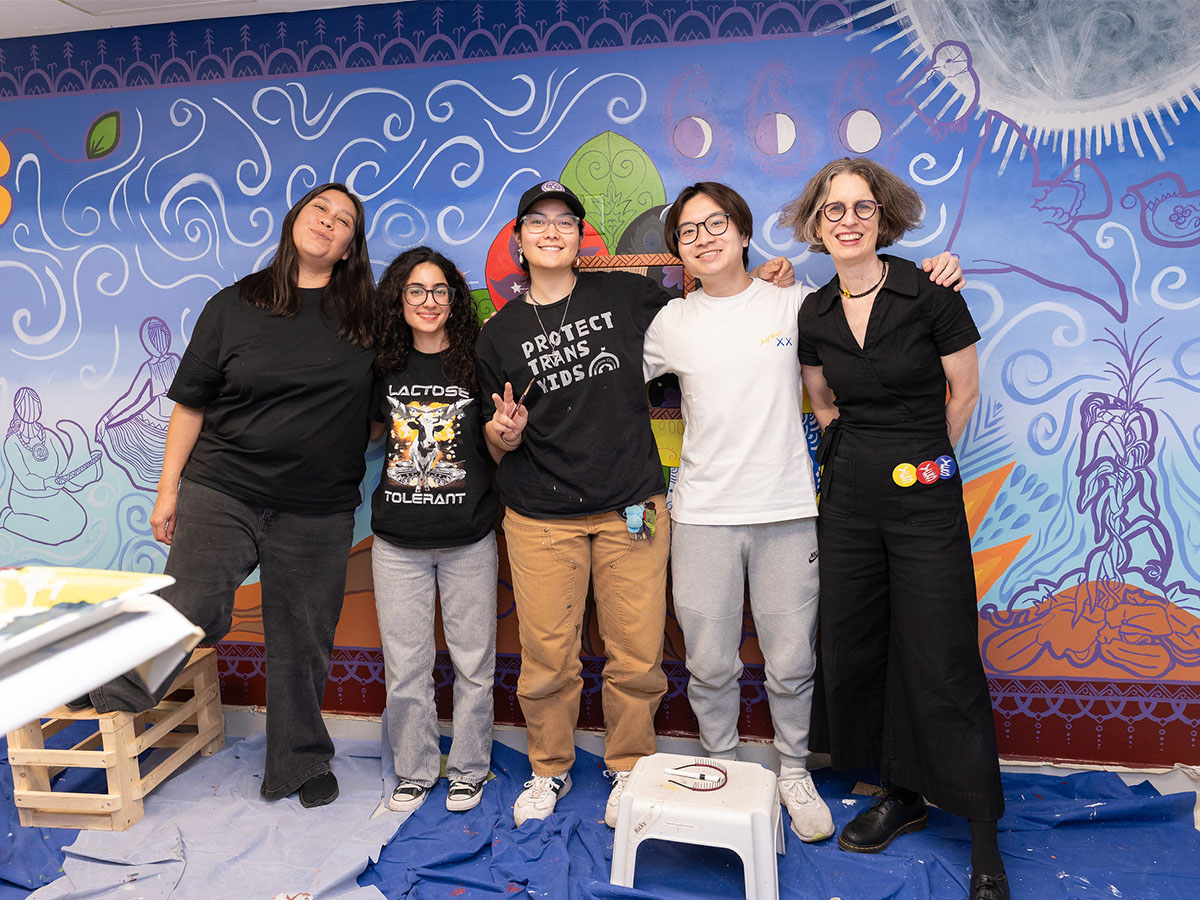 Lisa Landrum standing with artists Giselle Del Vallé and Ange Loft in front of Onkwe’shón mural at Toronto Metropolitan University’s Department of Architectural Science.