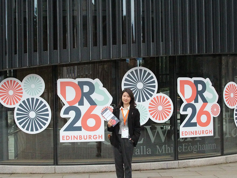Yaxin Jiang standing in front of colourful DRS26 conference signage in Scotland.