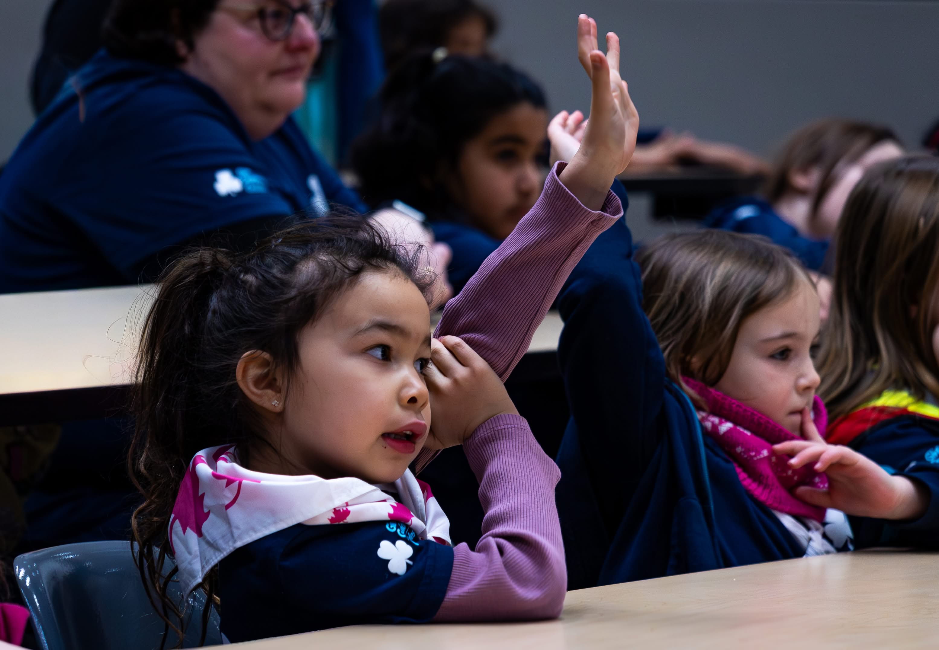 Two Girl Guides wearing bandanas and holding up their hands.