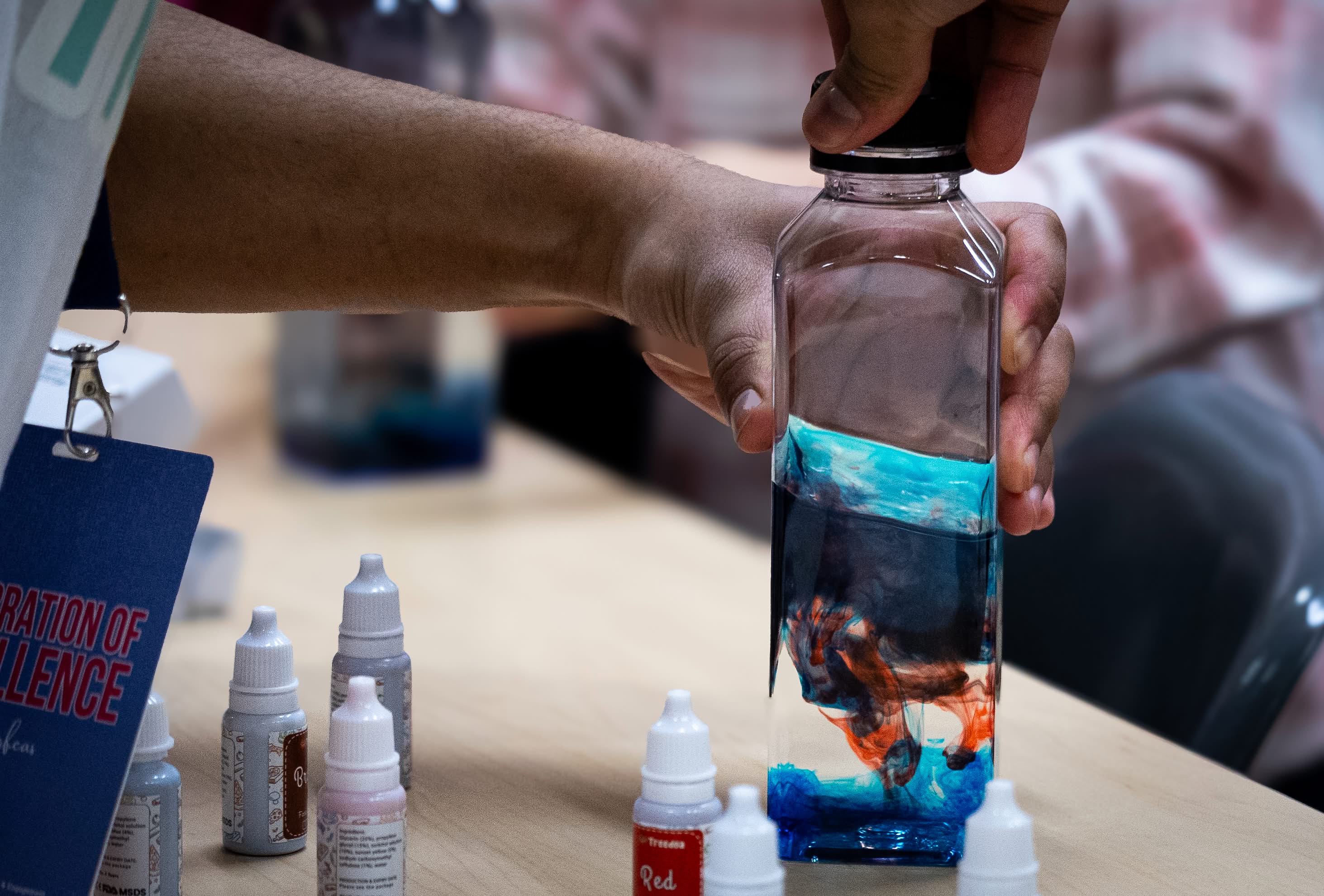 A hand holds a glass bottle containing a fluorescent blue liquid.