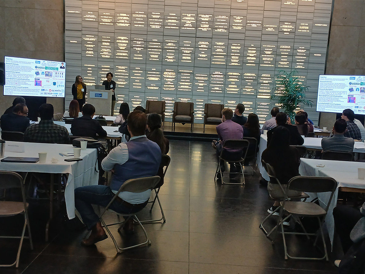 Professors Hadis Zarrin and ChungHyuk Lee presenting to a group of people in the auditorium. 