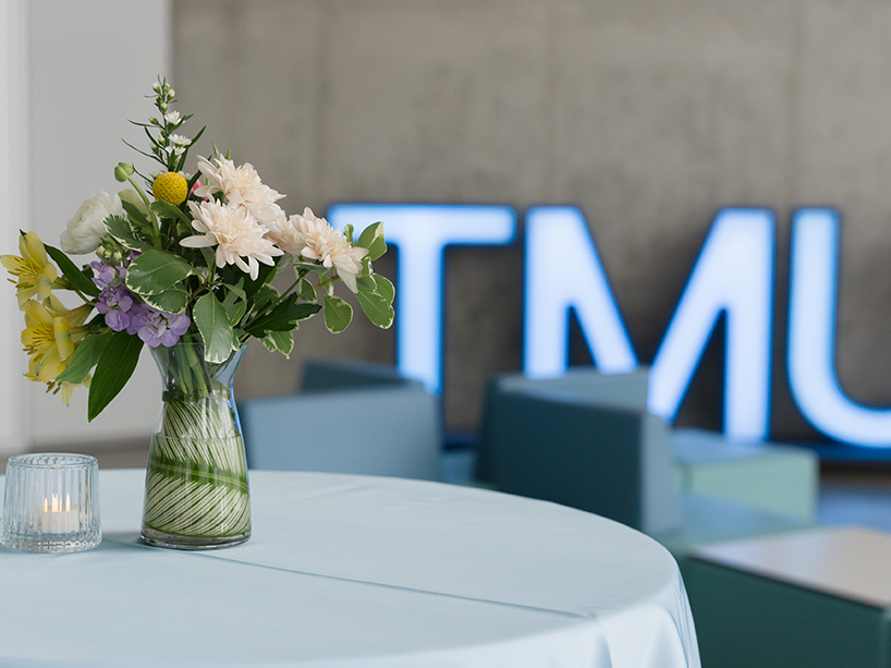 A flower vase on a white tablecloth with TMU light-up letters standing behind.