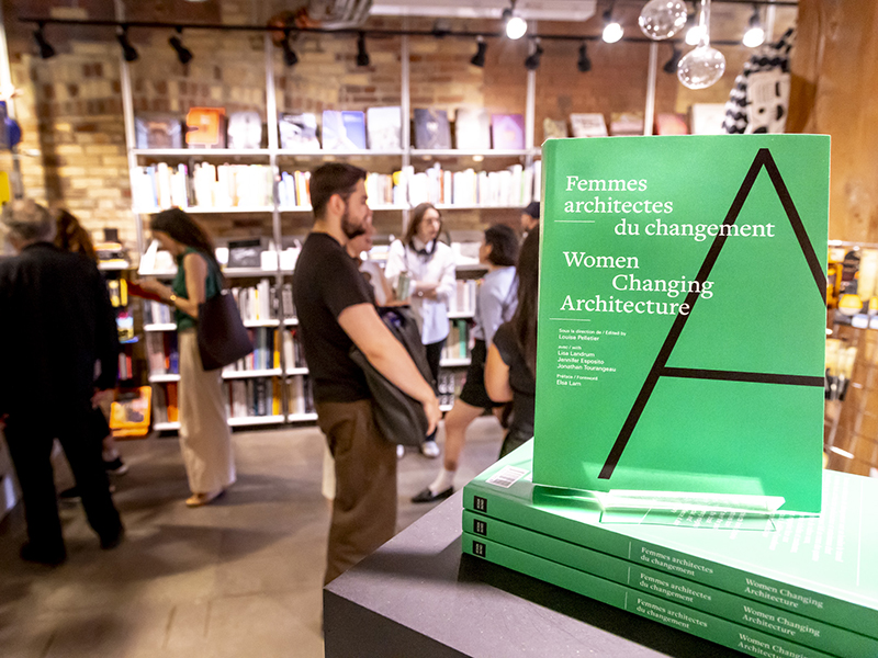  A stack of bright green books inside a bookstore with people reading in the background.