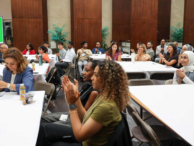 Audience members clap and cheer while seated at tables during the presentations.