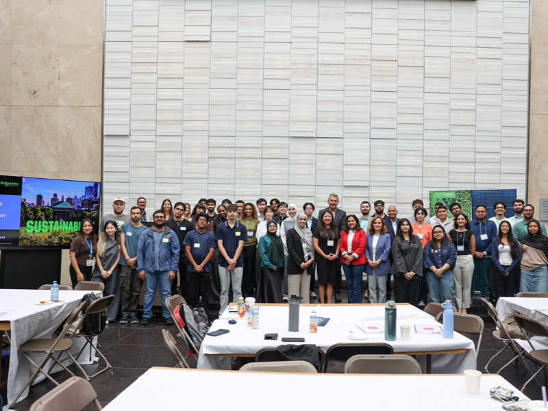 Schneider Electric employees, co-op students, and TMU staff pose together on stage for a group photo.