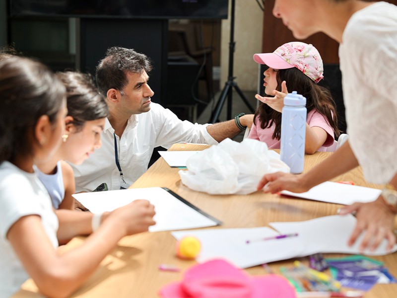 An event host listens closely to a student attendee speaking at a worktable.
