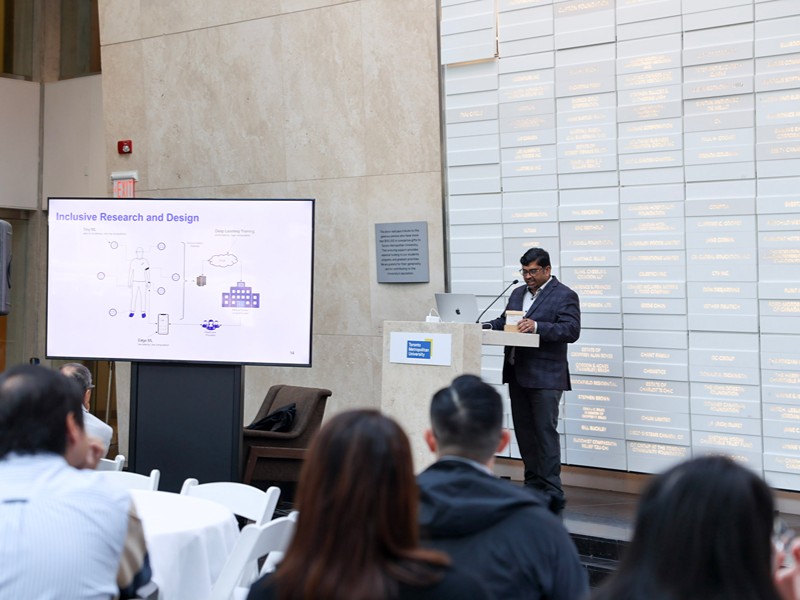 Dr. Sri Krishnan presents on stage next to a slide titled "Inclusive Research and Design". 