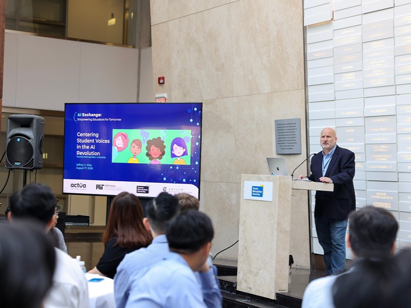 Jeffrey C. Riley presents at a podium next to a slide titled "Centering Student Voices in the AI Revolution".