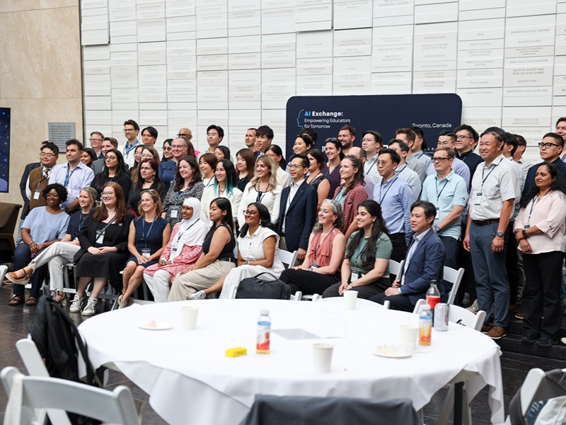 A large group of TMU, Actua, and MIT RAISE event attendees poses together in front of the AI Exchange banner.