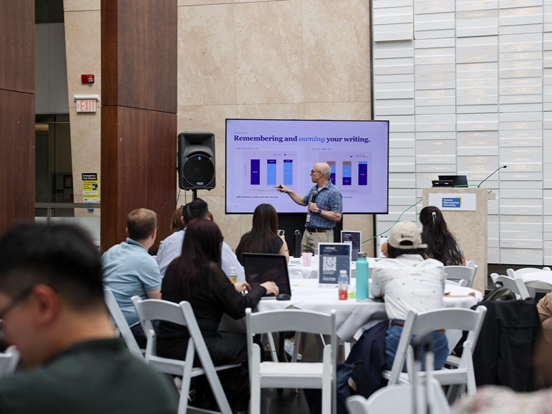 A speaker presents a slide deck session to seated audience members during the conference.  