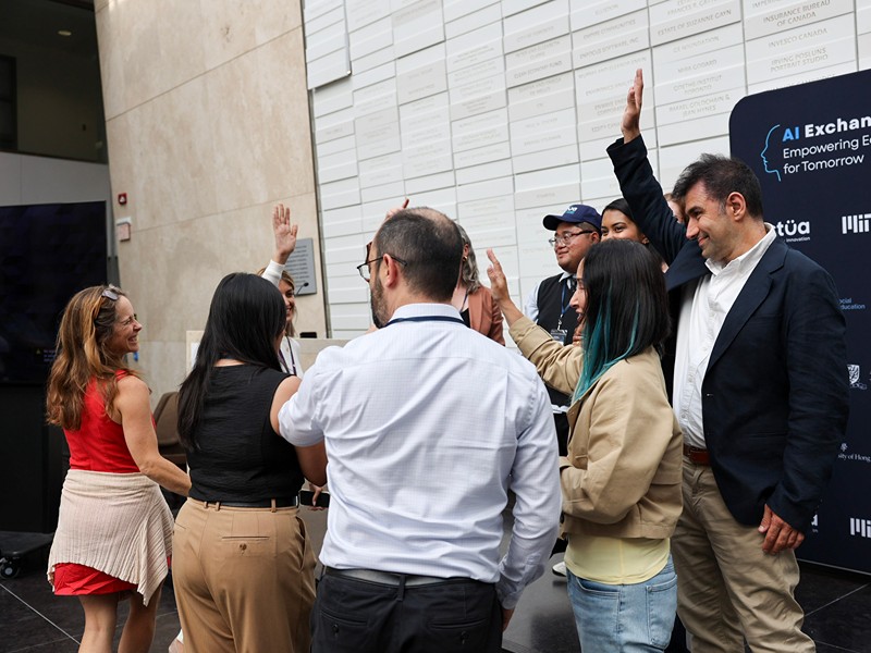 Actua, MIT RAISE, and TMU staff gather in a circle, smiling and raising their hands to celebrate. 