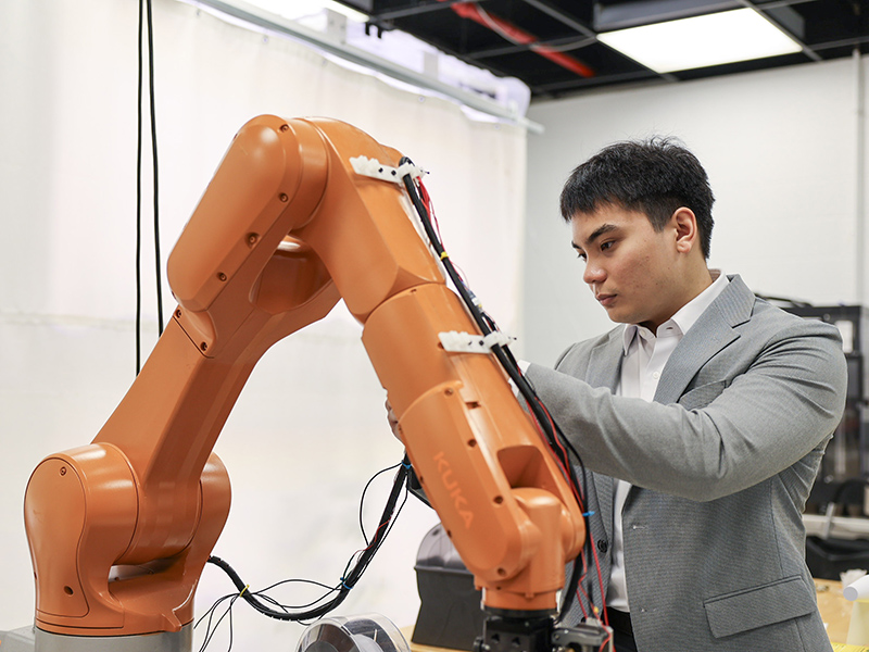 TMU graduate studies engineering student wearing blazer working on orange robotic arm in lab.