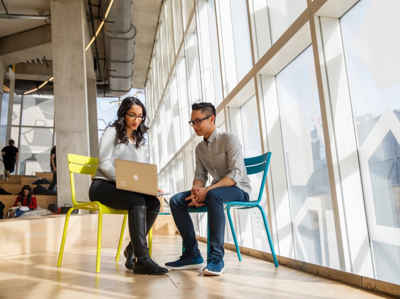 Two people working together on a laptop by a window.
