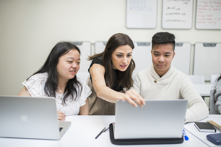 Instructor engaged in a discussion with students while looking at laptop monitor