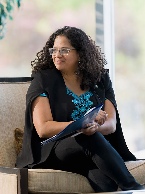 Dr. Tanya (Toni) De Mello sitting with a folder and pen in her hand listening to someone speaking