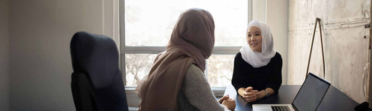 Muslim woman wearing a hijab in conversation with a colleague.