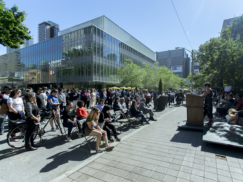 TMU community members gather on Gould Street, listening to a person at a podium at the plaque unveiling for next to the Egerton TMU statue on Gould Street 