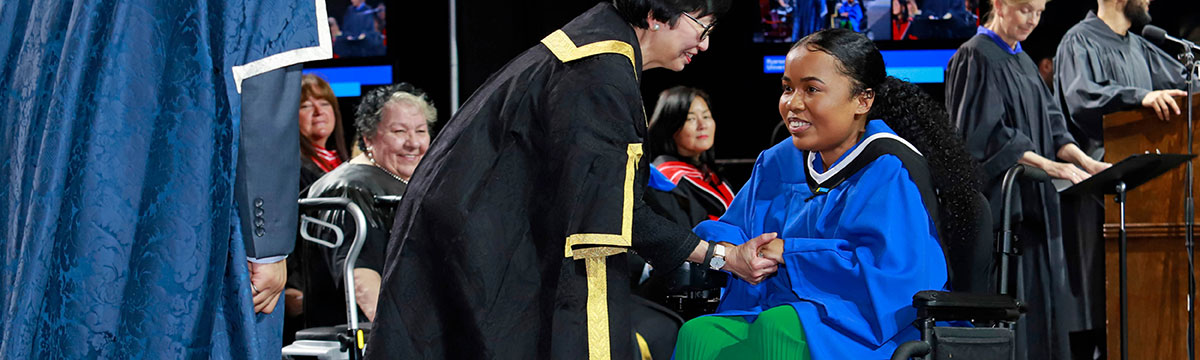 Black student in wheelchair receiving diploma on stage at convocation