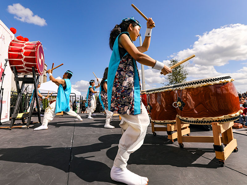 Several Asian people dressed in ceremonial clothing beating drums