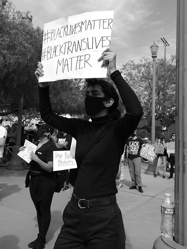 A person wearing a mask holding a sign marked. Black Lives Matter, Black Trans Lives Matter.