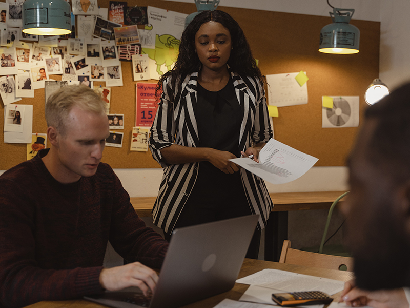 A person standing with two other people sitting at computers