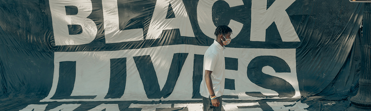 A Black person walking by a banner image that say Black Lives Matter