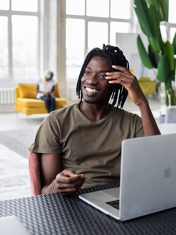 A Black man sitting smiling in front of a laptop