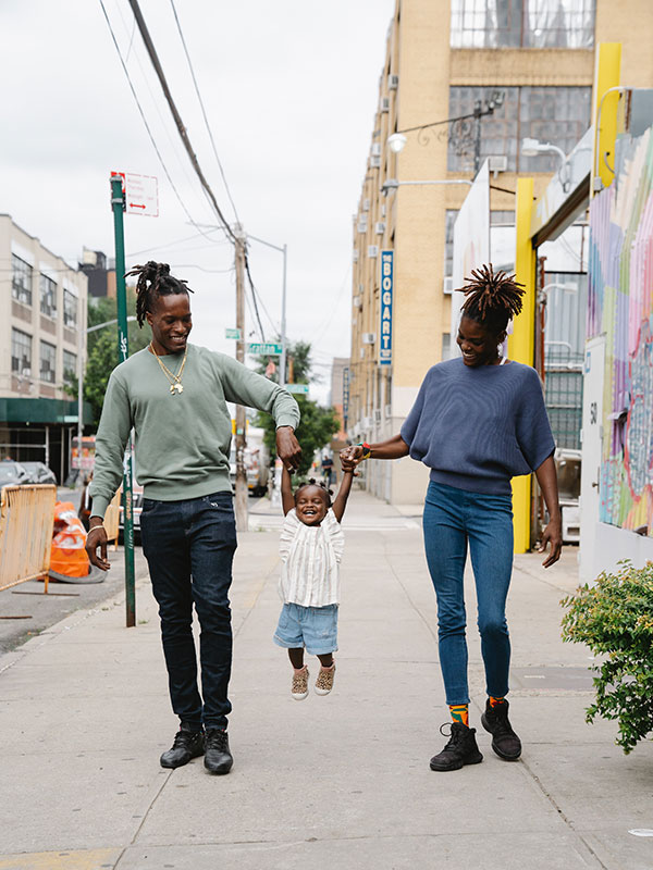 Two Black people swinging a child in the air by their hands