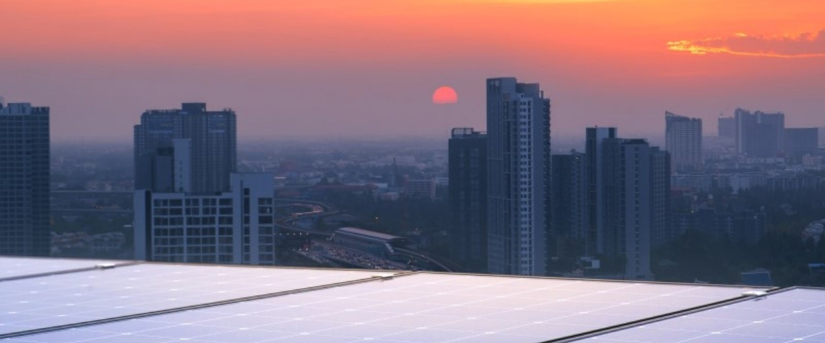 A city skyline is seen from the roof of a tall building as the sunsets.