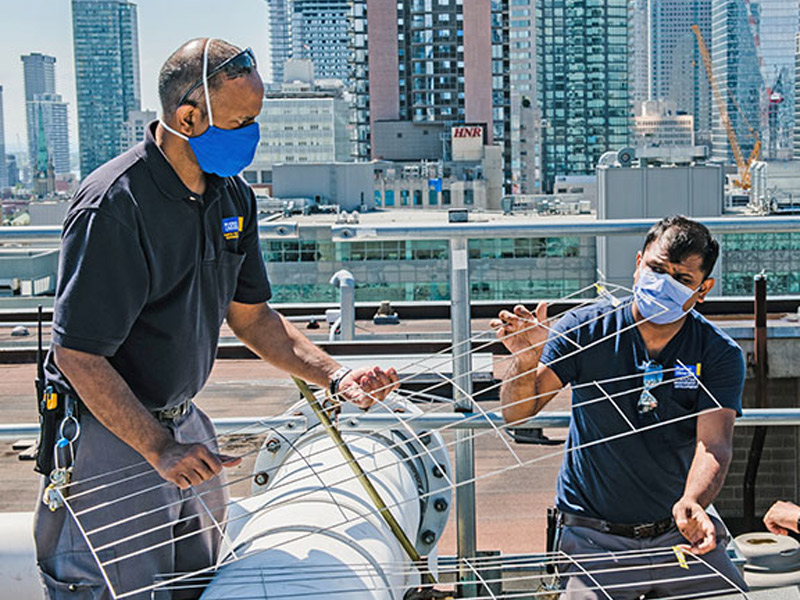 Two M&O staff work on a rooftop unit HVAC unit.