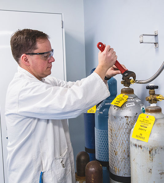 A departmental safety officer using a wrench to tighten the valves on equipment in the chemistry lab.