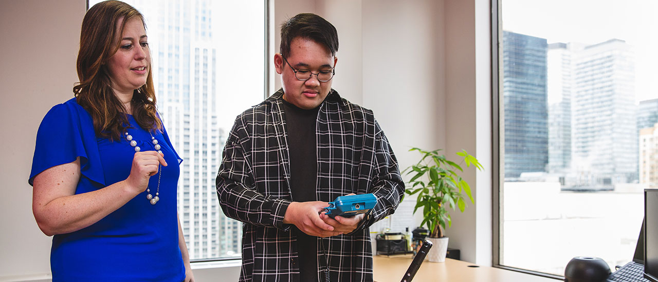Two members of the Environmental Health and Safety team checking a small meter in an office.