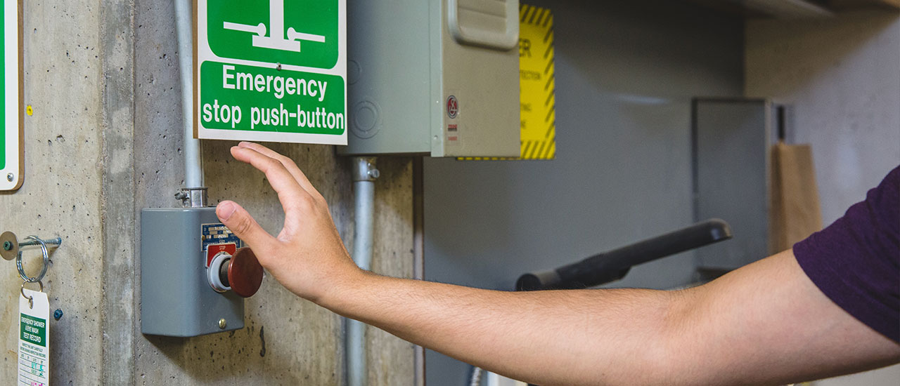 A hand reaching for the emergency stop button in a workshop. 