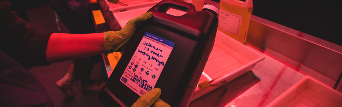 A person in a darkroom filling out a chemical label.