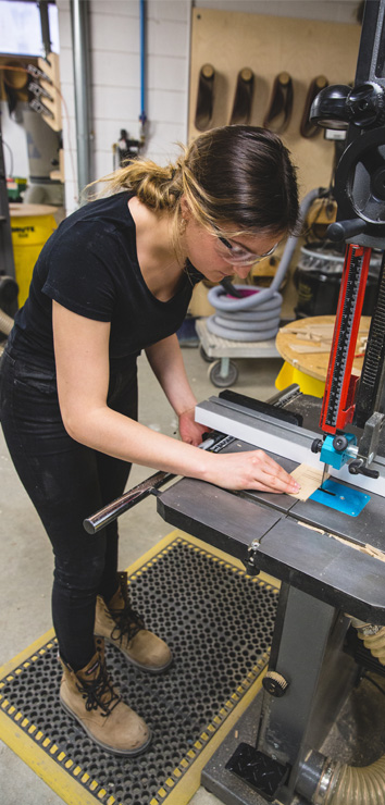 A woman cutting a small piece of wood with a saw while wearing safety glasses.